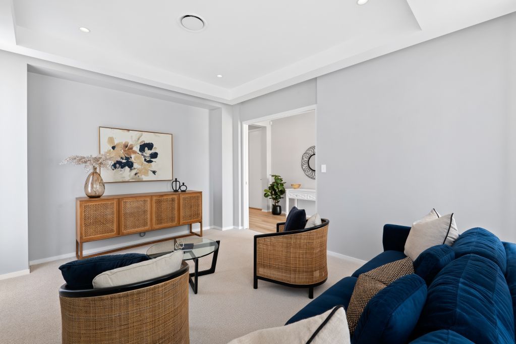 Modern living room with rattan chairs, blue sofa, wooden sideboard, and bright gray walls