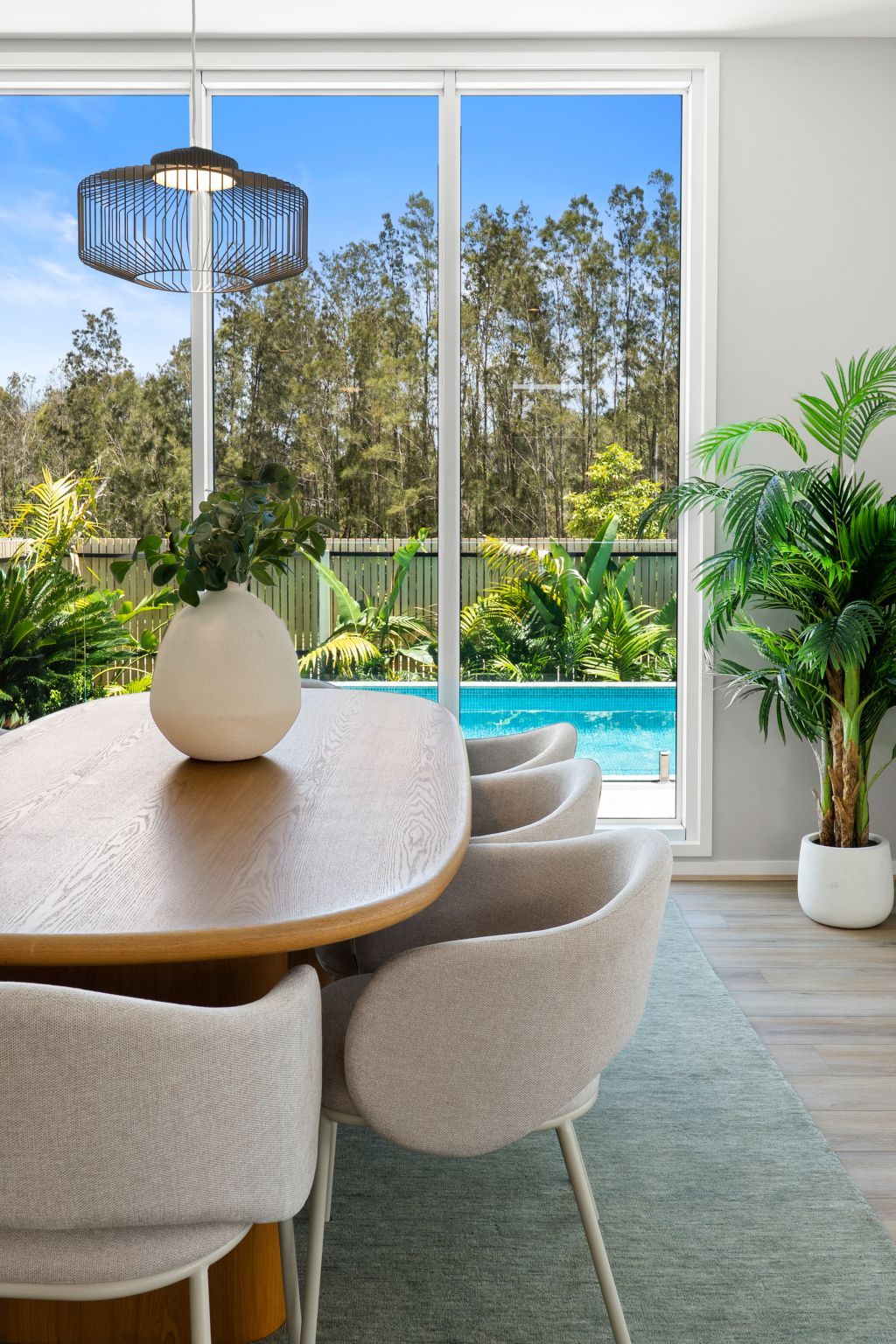 Modern dining room with a round table, beige chairs, and a pool view through large windows