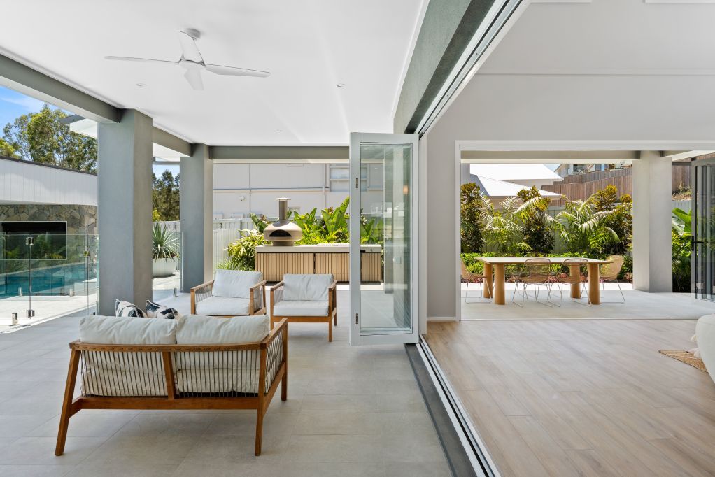 Modern covered patio with wicker seating and sliding glass doors overlooking a pool and garden