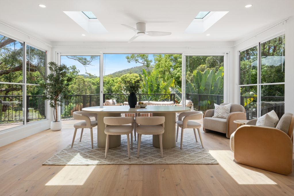 Bright sunroom dining area with large windows, wooden table, chairs, and garden view