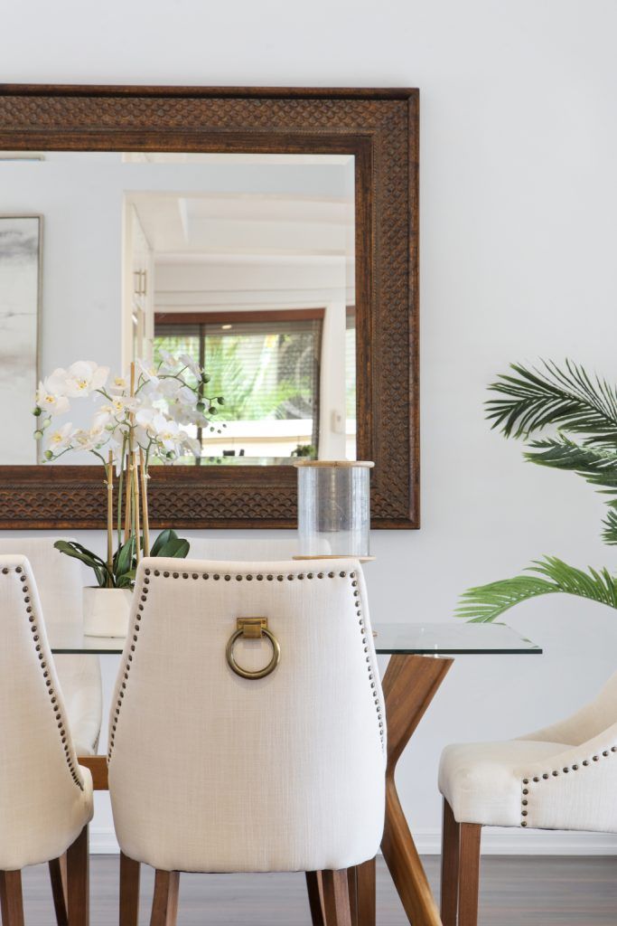 A dining room with a table and chairs and a large mirror on the wall.