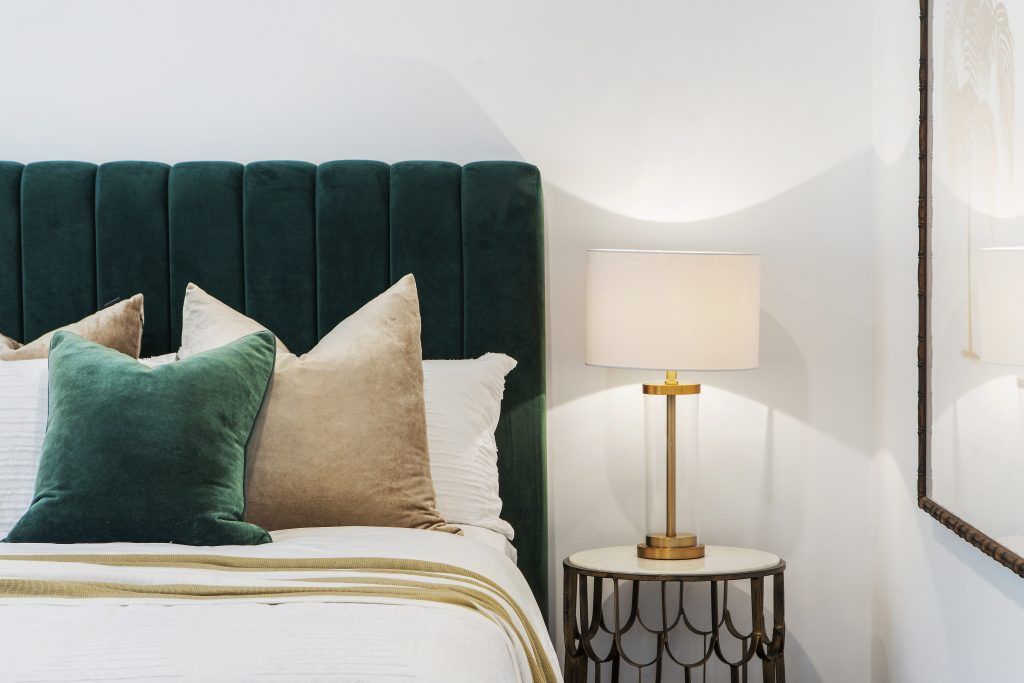 A bedroom with a bed , nightstand , lamp and mirror.