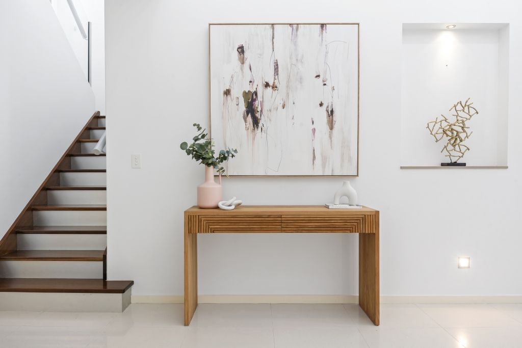 A wooden table with a vase of flowers on it is in a hallway next to a staircase.