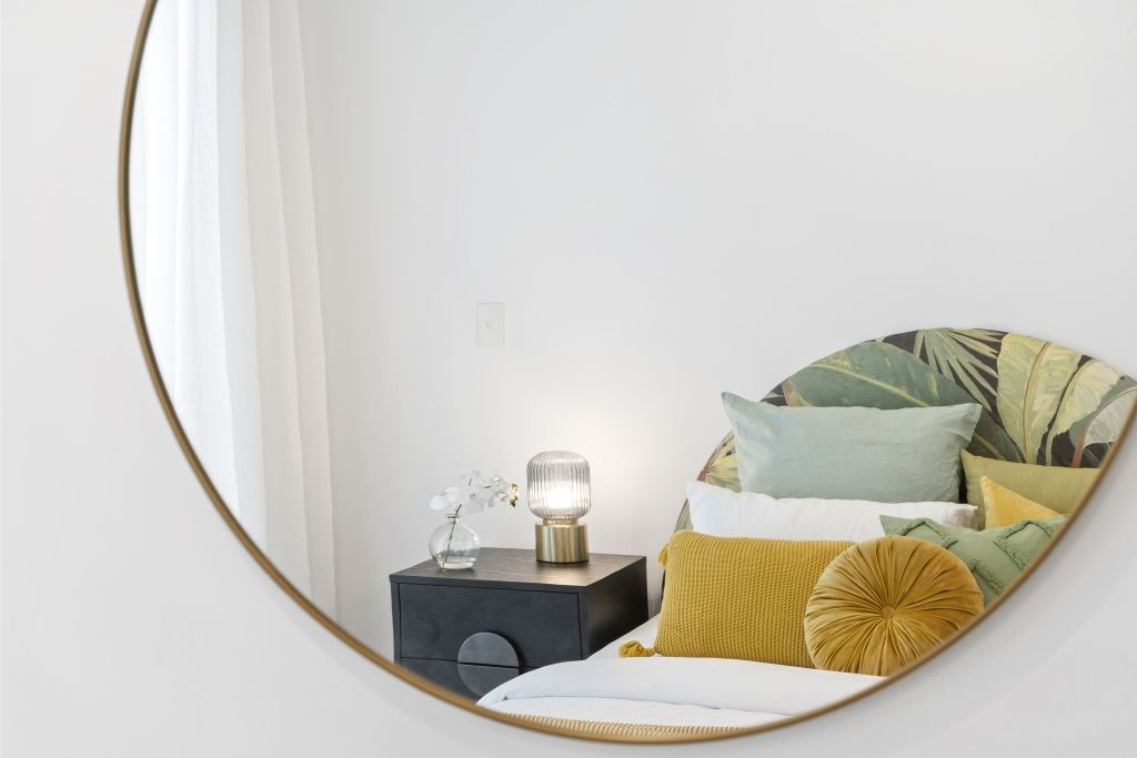 A bedroom with a bed , nightstand , mirror and lamp.