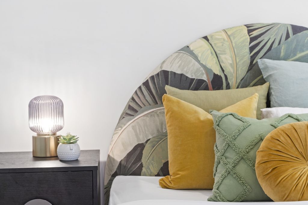 A bedroom with a bed , nightstand , lamp and pillows.