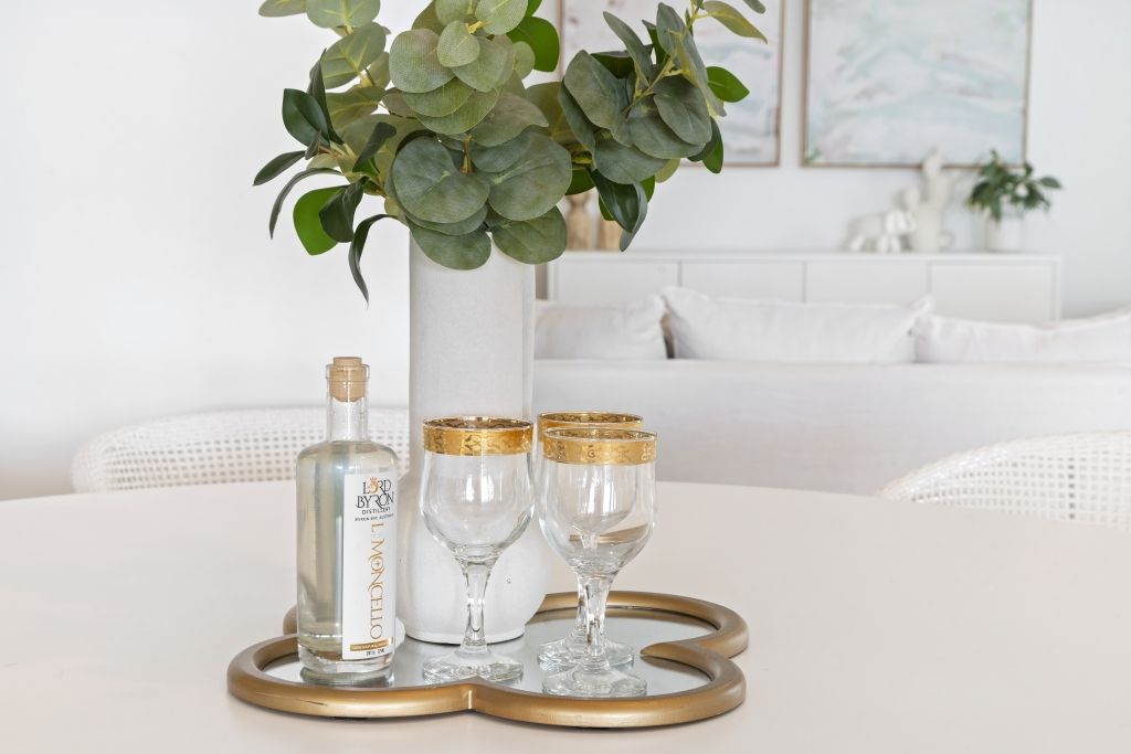 A tray with a vase of flowers and wine glasses on it is on a table.