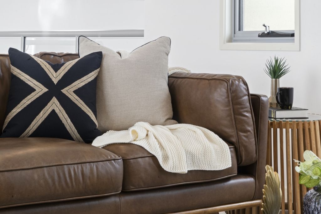 A brown leather couch with a black and white pillow on it