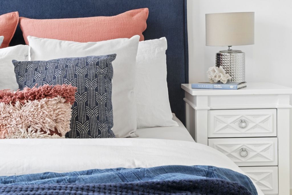 A bedroom with a bed , nightstand , lamp and pillows.