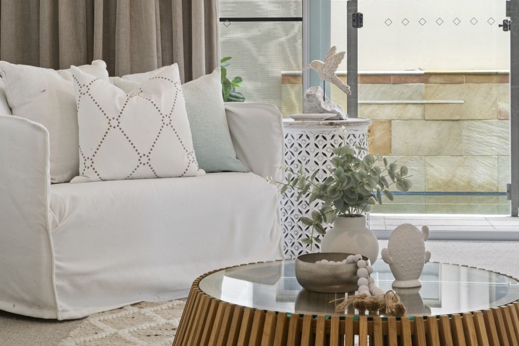 A living room with a white couch and a glass coffee table.