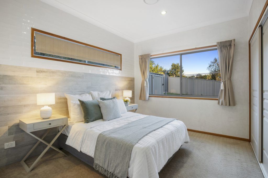 A bedroom with a bed , nightstand , lamps and a window.