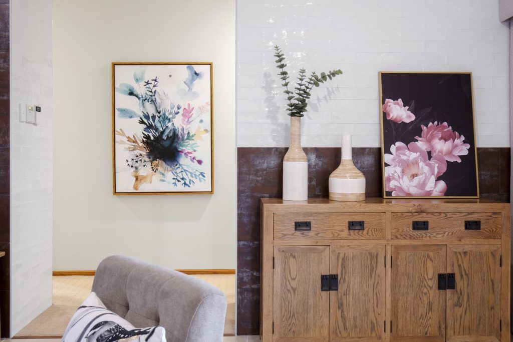 A living room with a couch , dresser , vases and paintings on the wall.