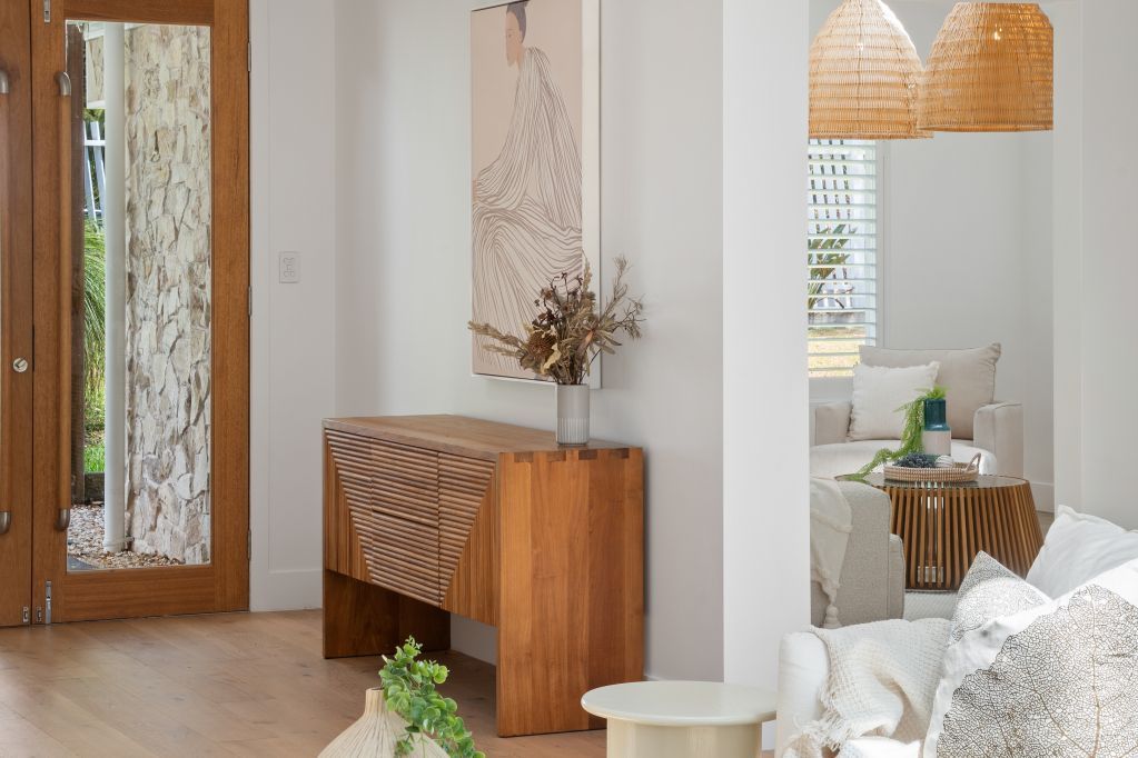 Bright entryway with wooden console, tall art, woven pendant lights, and a glimpse of a living room.