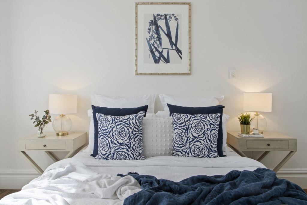 A bedroom with a bed , nightstands , lamps and a picture on the wall above the bed.