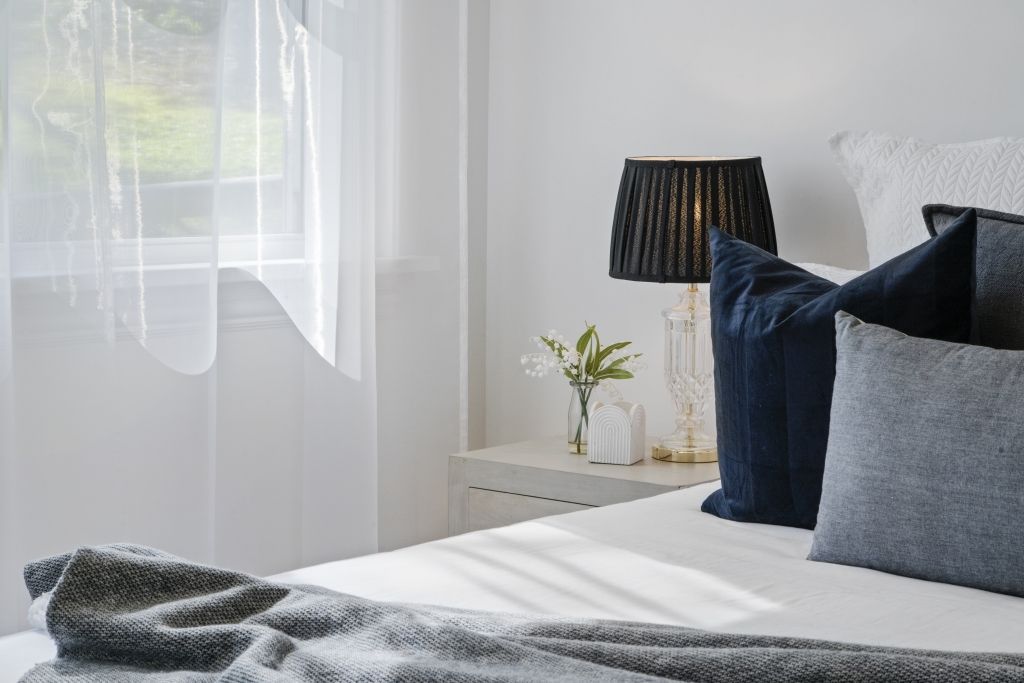 A bedroom with a bed , pillows , a lamp and a window.