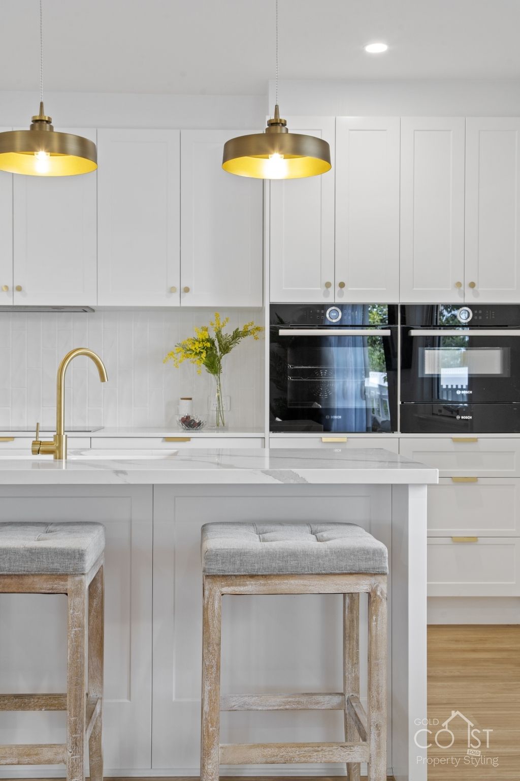 A kitchen with white cabinets , stools , a sink and two ovens.