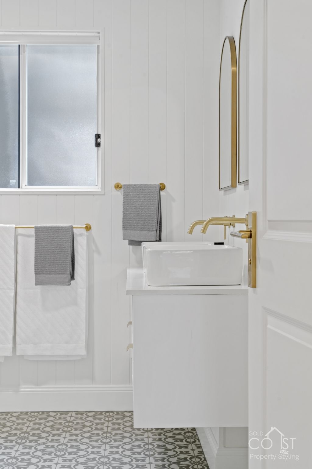 A bathroom with a sink , mirror , towels and a window.
