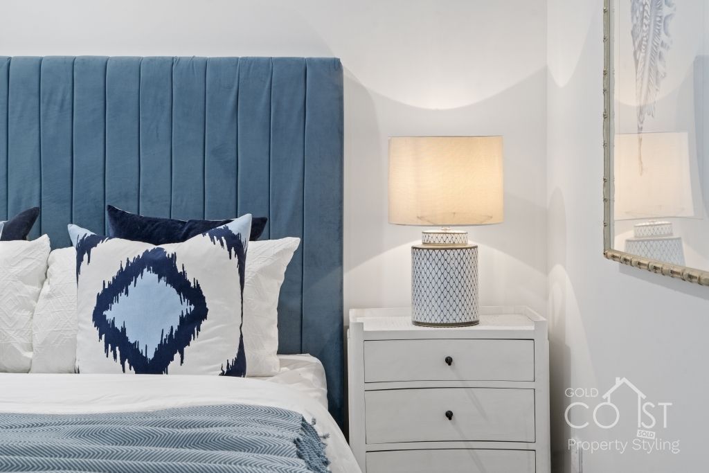 A bedroom with a bed , nightstand , lamp and picture on the wall.