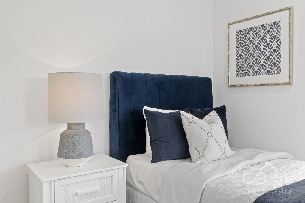 A bedroom with a bed , nightstand , lamp and picture on the wall.
