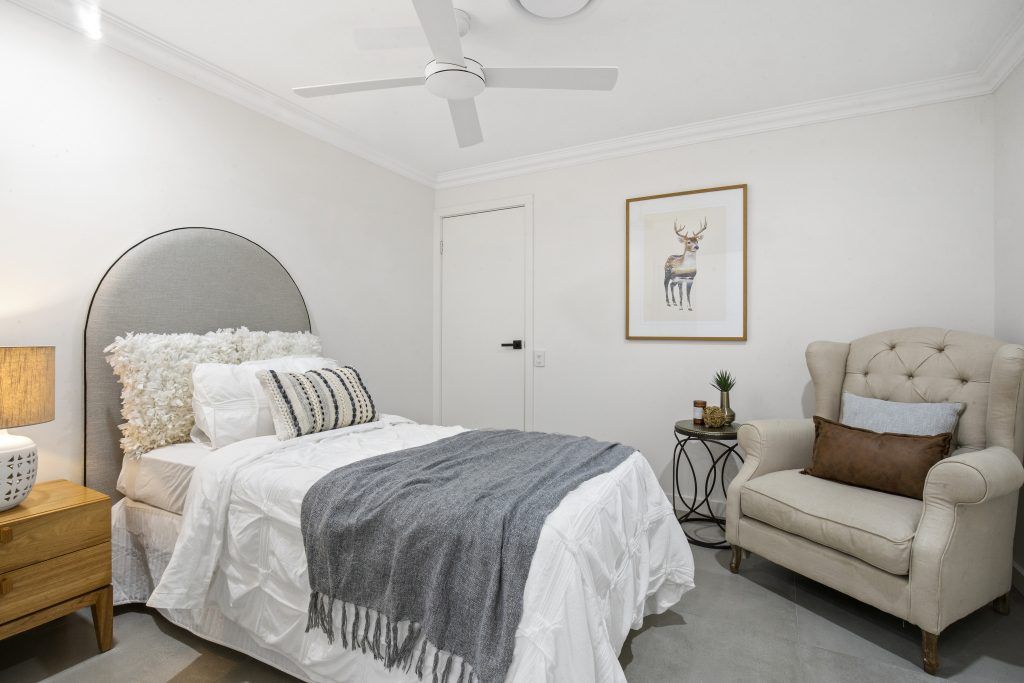 A bedroom with a bed , chair , nightstand and ceiling fan.