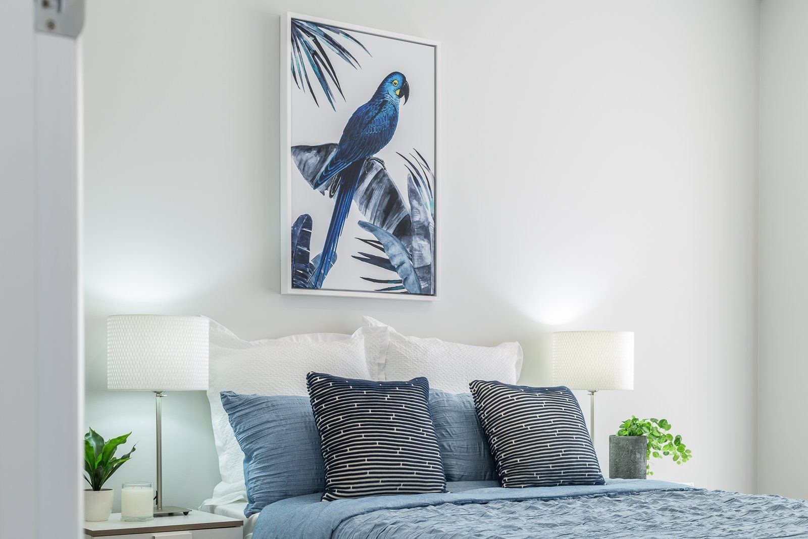 A bedroom with a blue parrot painting on the wall above the bed.