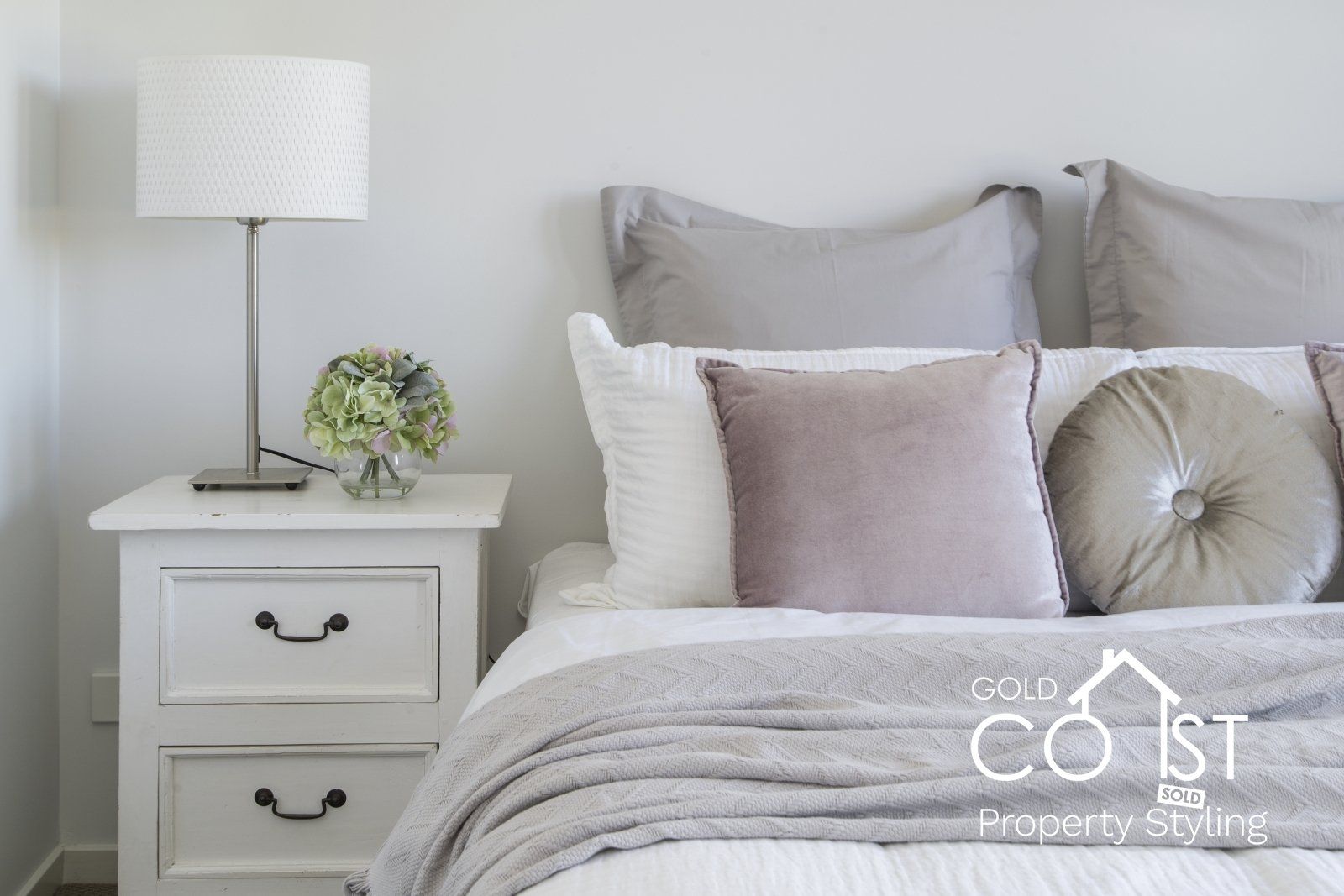 A bedroom with a bed , nightstand , lamp and coast property styling logo