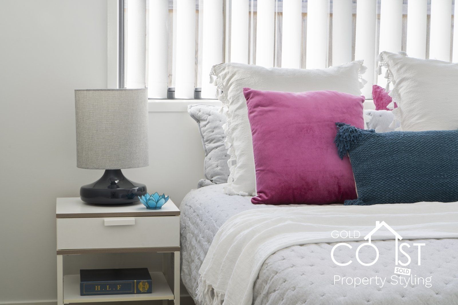 A bedroom with a bed , nightstand , lamp and pillows.