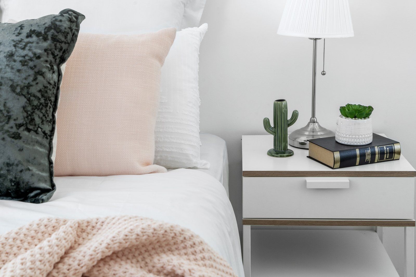 A bedroom with a bed , nightstand , lamp and pillows.