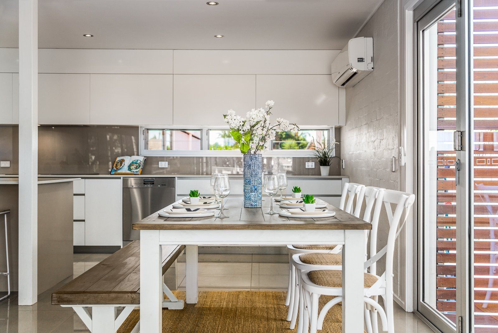 A dining room table and chairs in a kitchen with a vase of flowers on it.