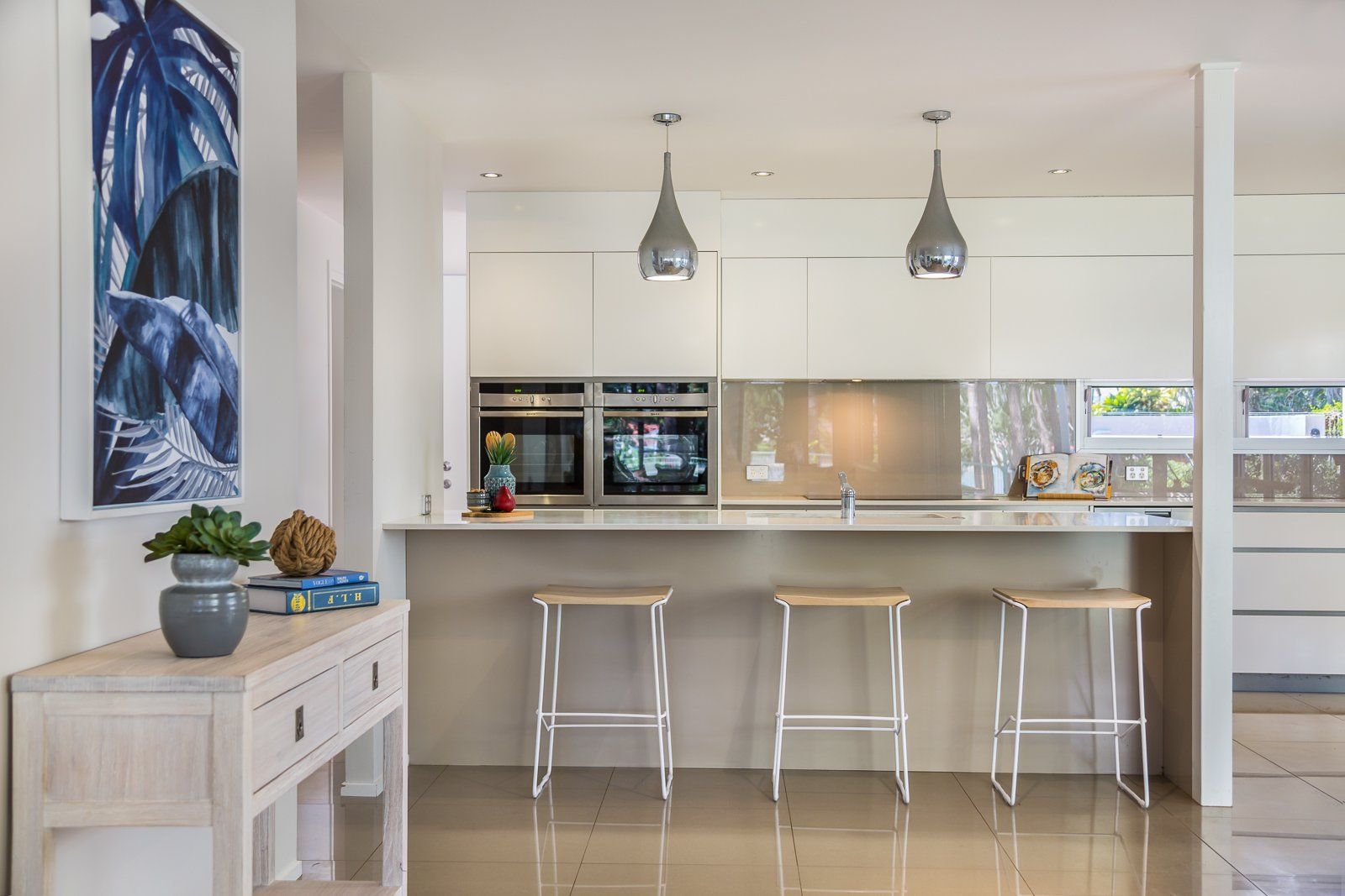 A kitchen with white cabinets , stools , a table and a painting on the wall.