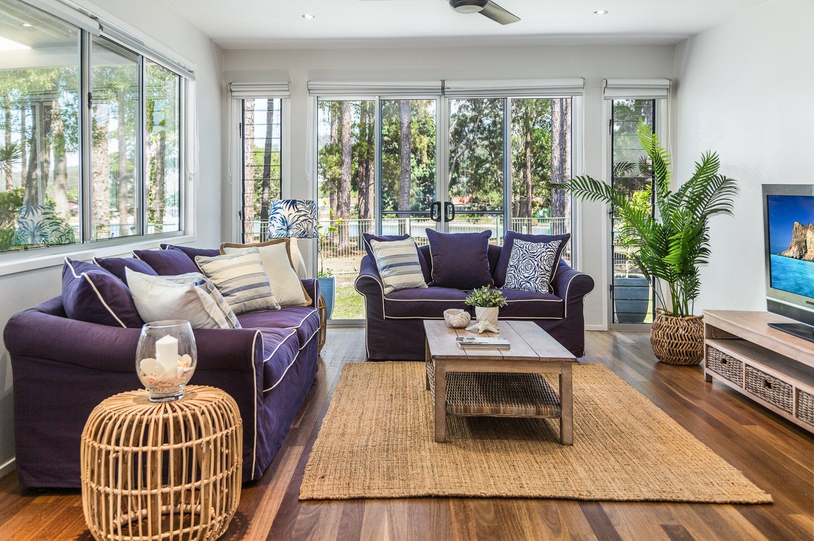 A living room with a purple couch , two chairs , a coffee table , and a television.