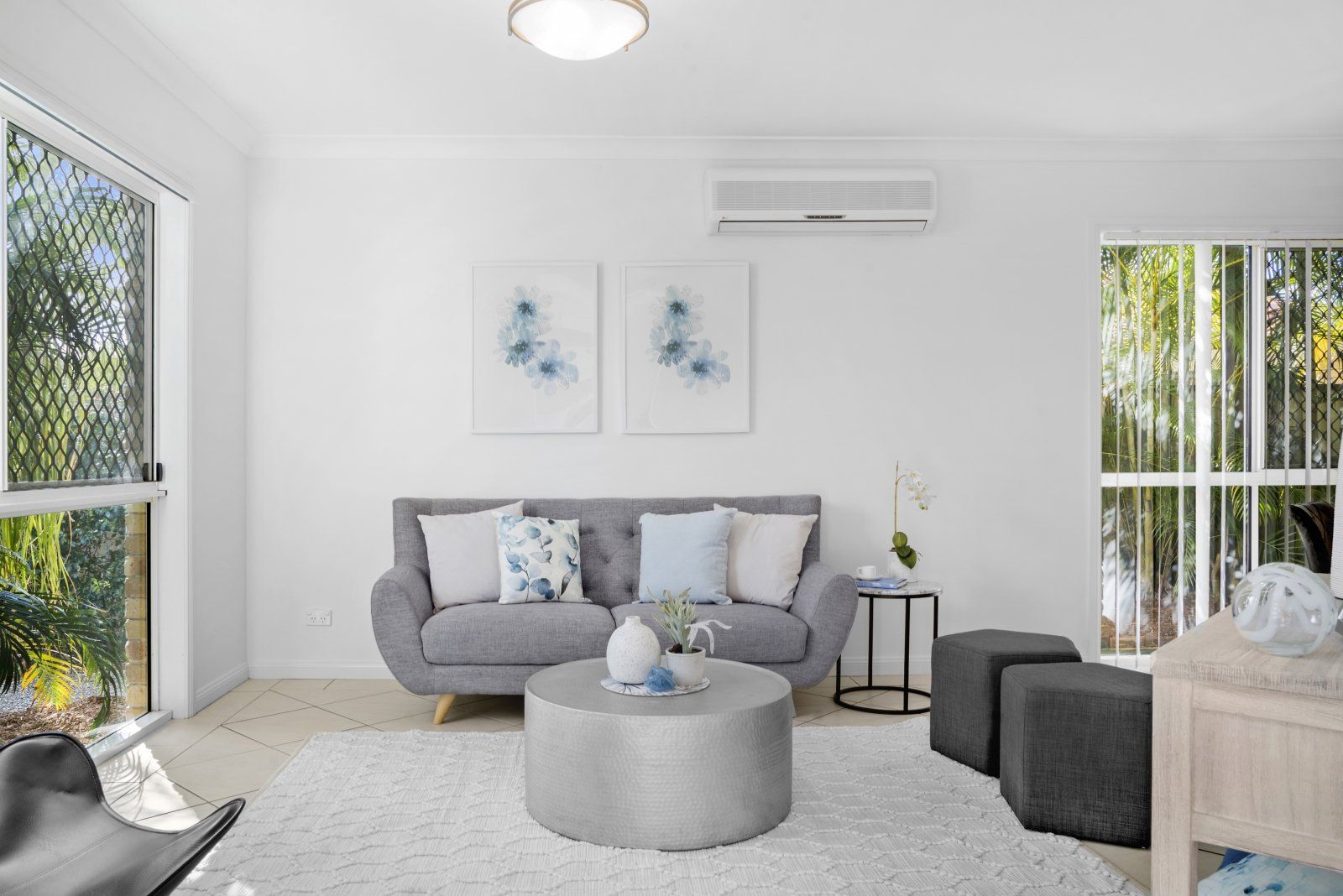 A living room with a couch , coffee table , ottomans and a large window.