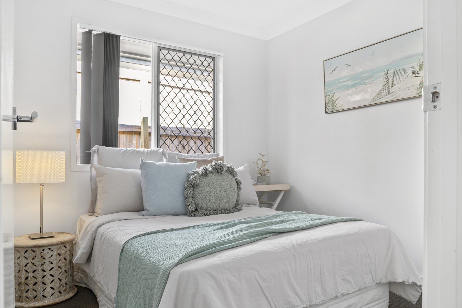 A bedroom with a bed , nightstand , lamp and window.