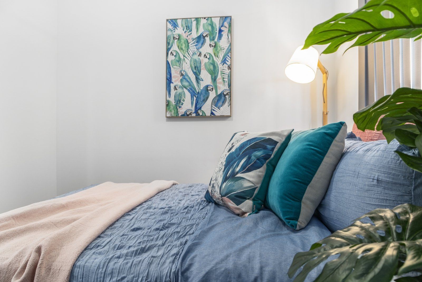 A bedroom with a bed , pillows , a lamp and a painting on the wall.