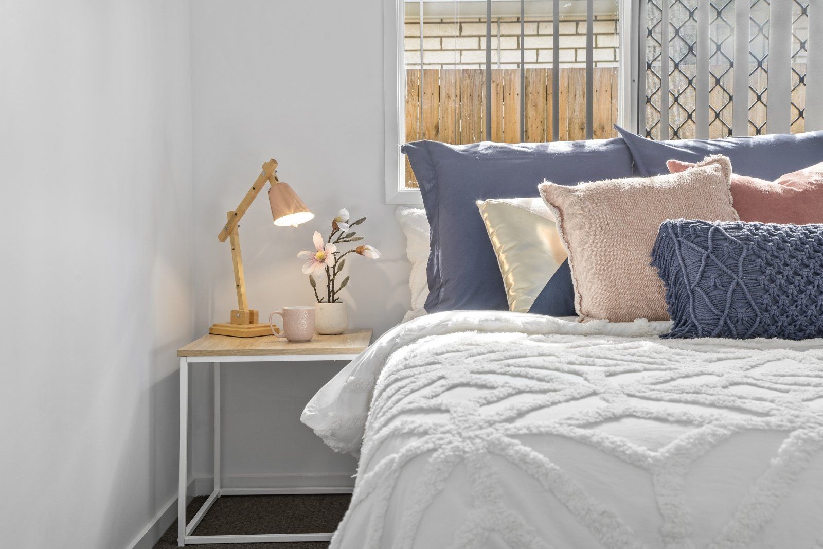 A bedroom with a bed , nightstand , lamp and window.