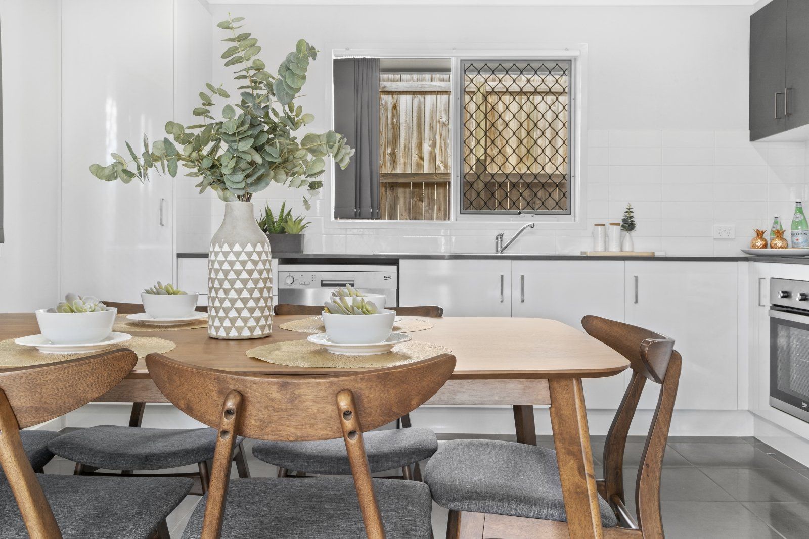 A dining room table and chairs in a kitchen with a vase of flowers on it.