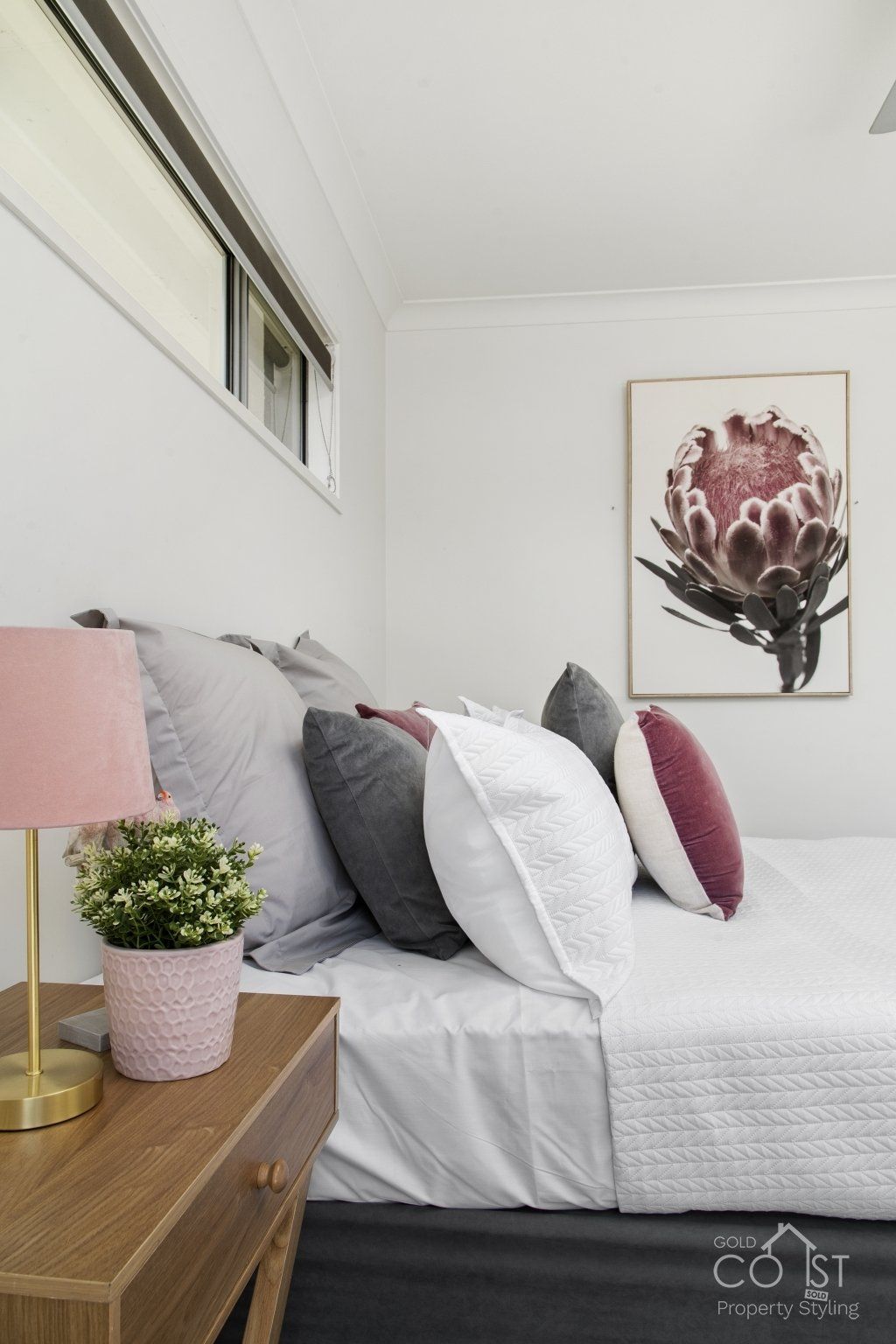 A bedroom with a bed , nightstand , lamp and painting on the wall.