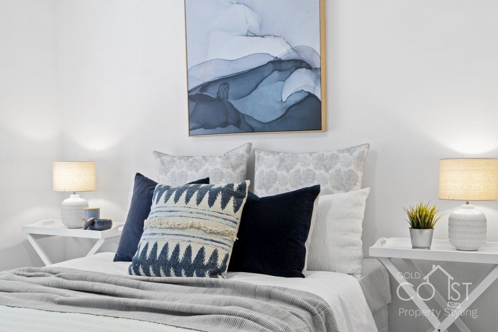 A bedroom with a bed , pillows , lamps and a painting on the wall.