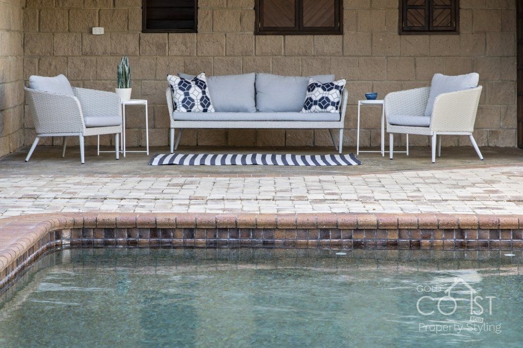 A patio with a couch and chairs next to a swimming pool.