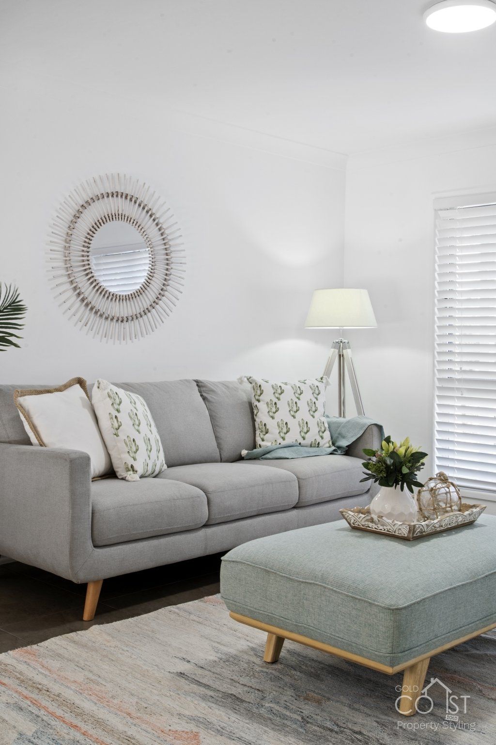 A living room with a couch , ottoman , coffee table and mirror.