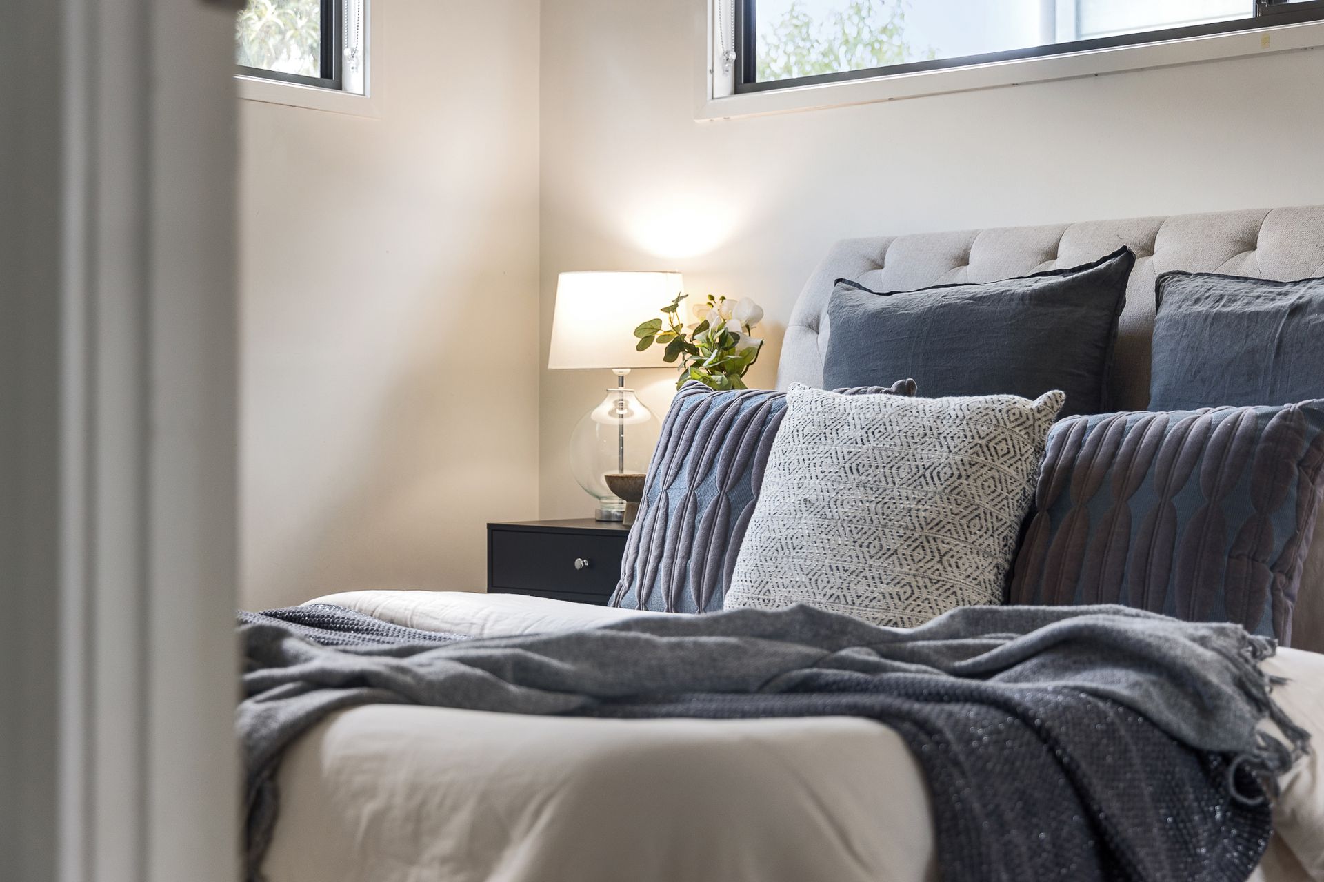 A bedroom with a bed , nightstand , lamp and window.