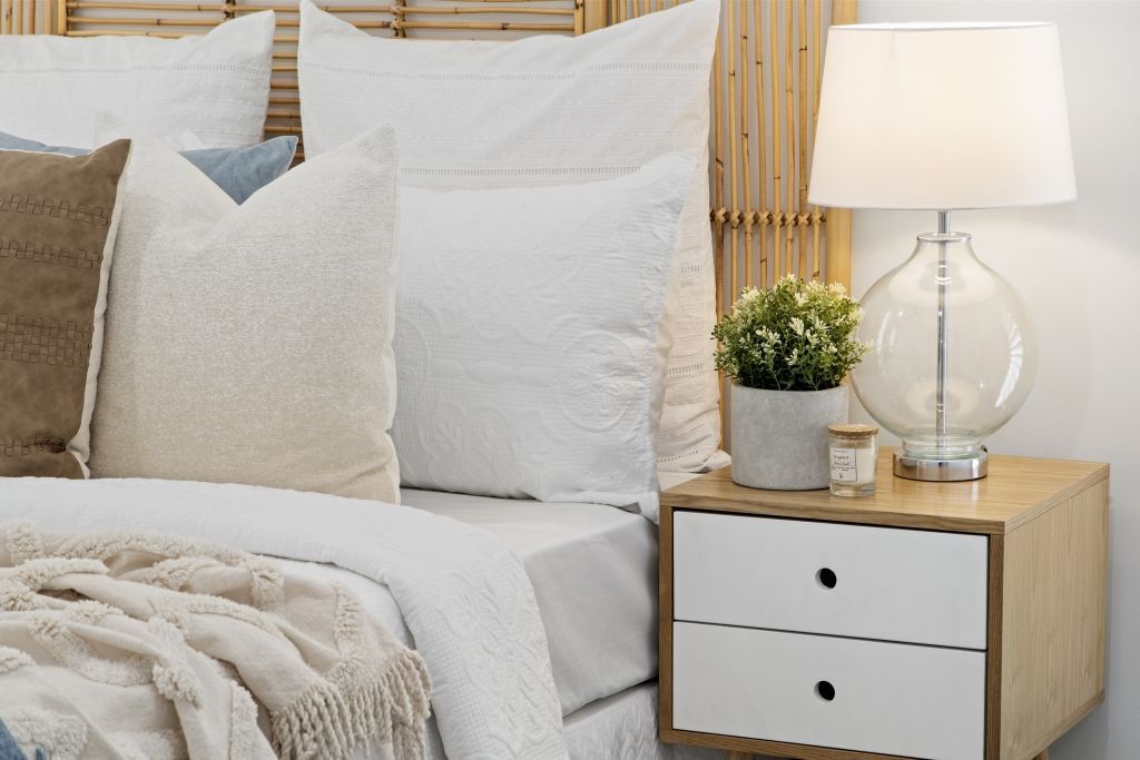 A bedroom with a bed , nightstand , lamp and plant.