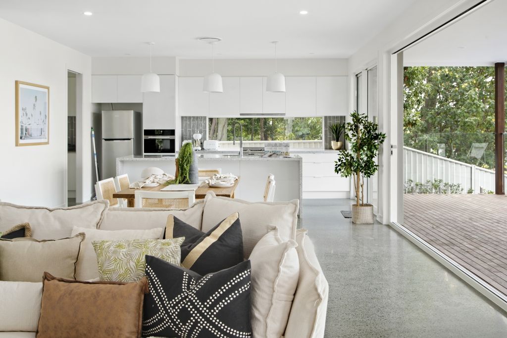 A living room with a couch and pillows and a kitchen in the background.
