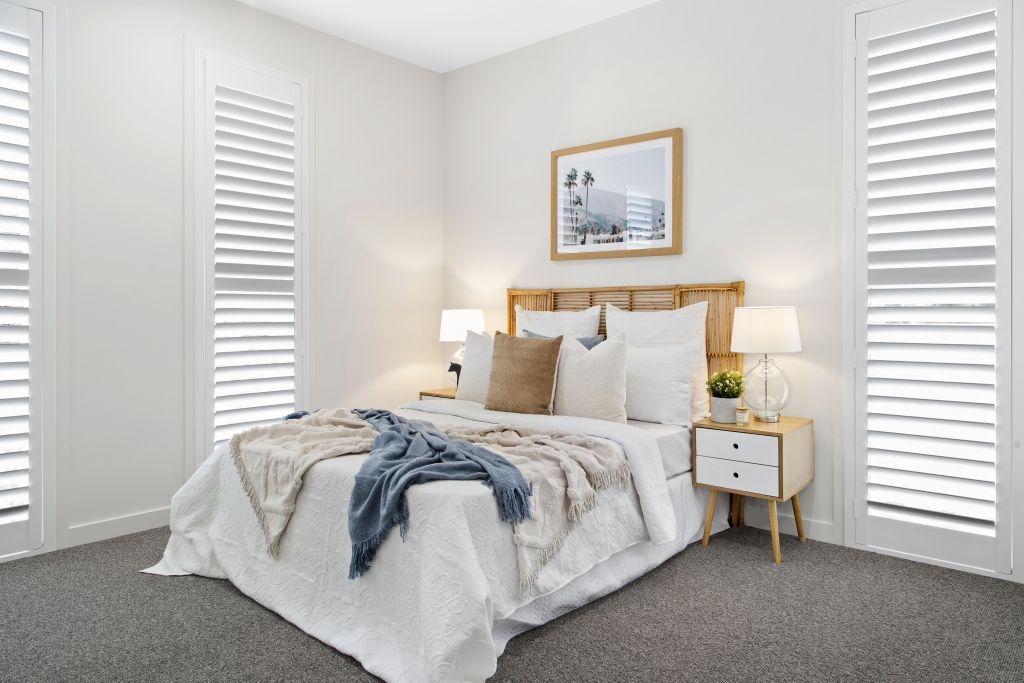A bedroom with a bed , nightstand , lamps and shutters.