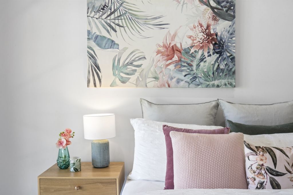 A bedroom with a bed , nightstand , lamp and a painting on the wall above the bed.