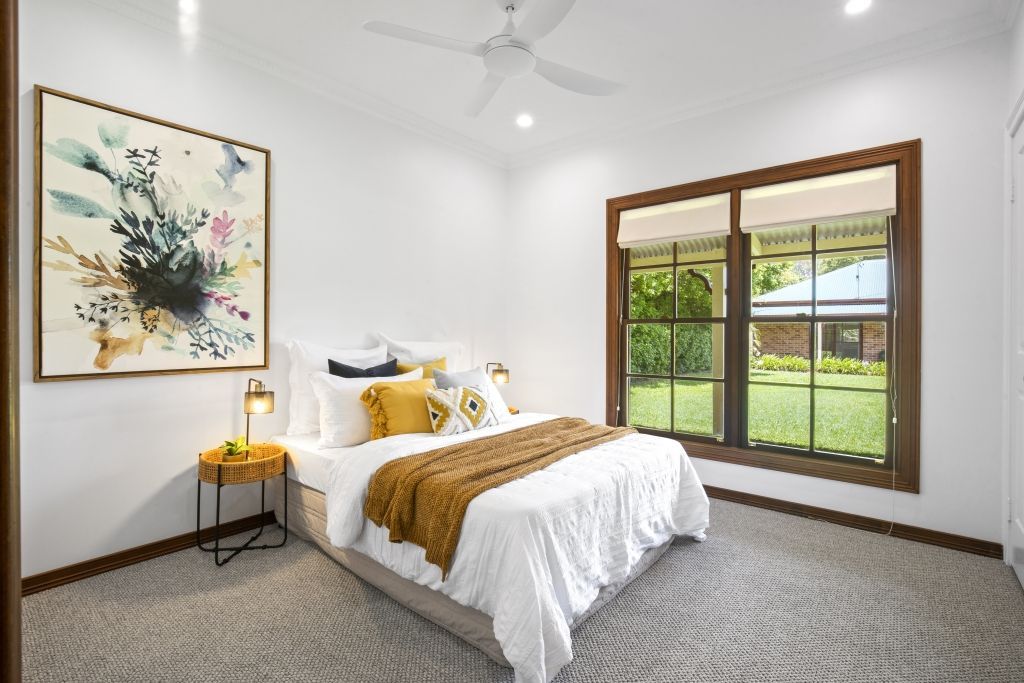 A bedroom with a bed , two windows , a ceiling fan and a painting on the wall.