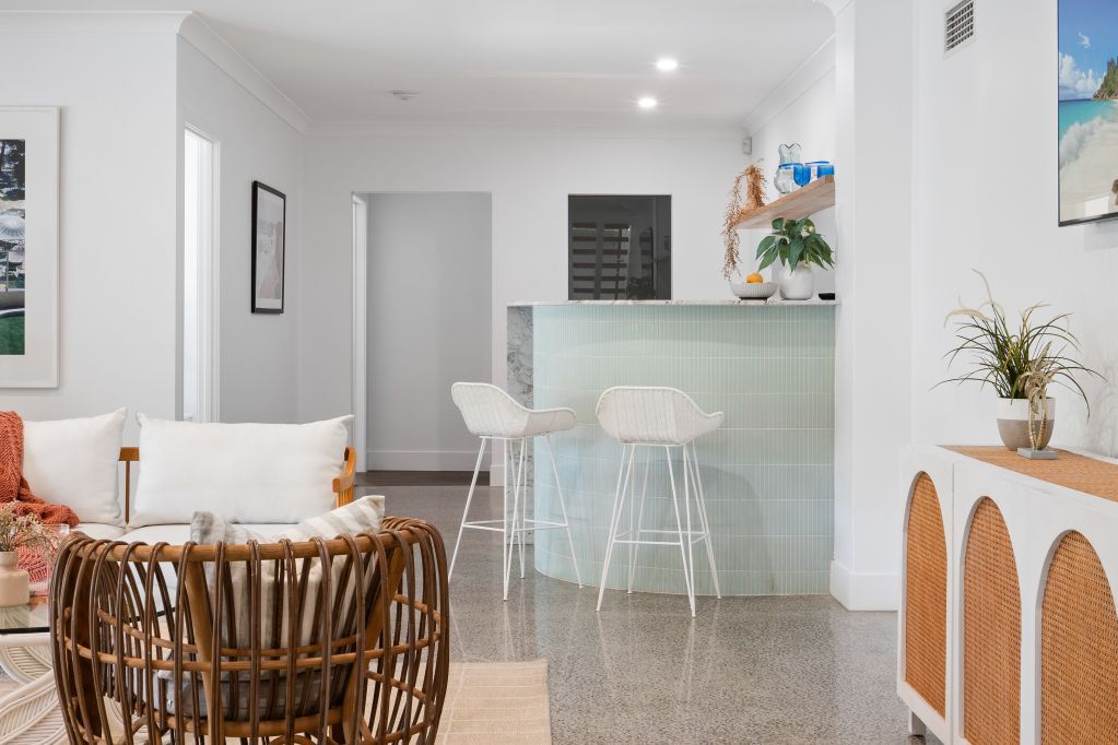 Bright modern living room with wicker chair, glass breakfast bar, and pale decor