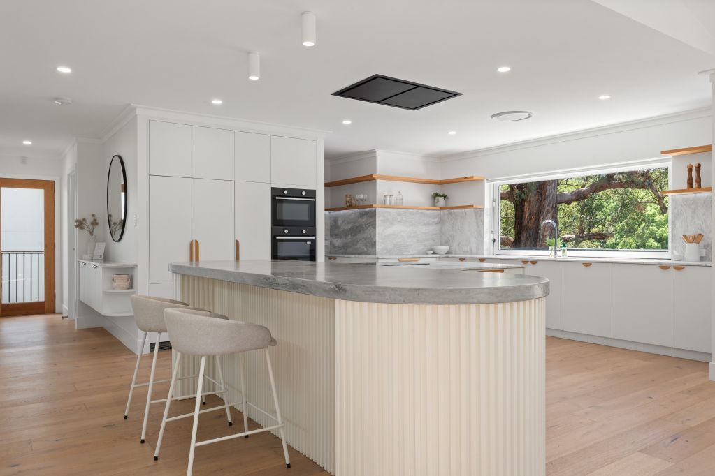 Bright modern kitchen with curved island, white cabinets, wood floors, and large window seating area