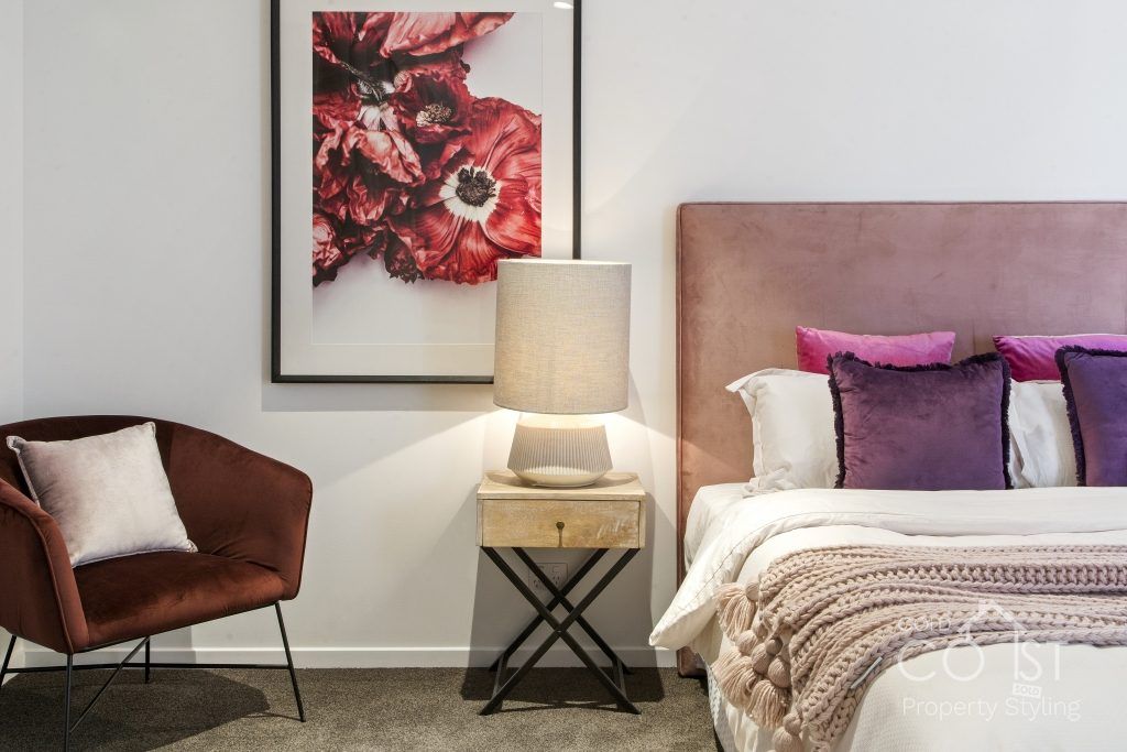 A bedroom with a bed , chair , nightstand , lamp and painting on the wall.