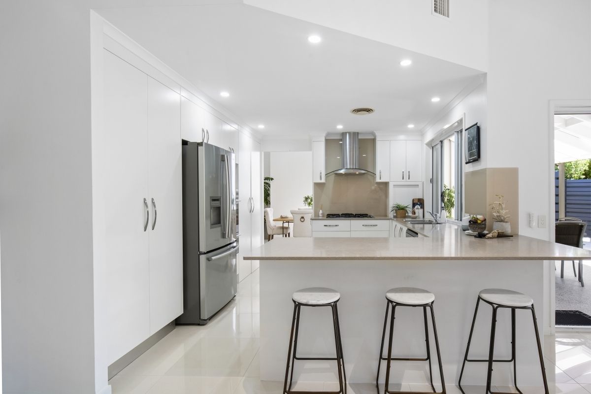 A kitchen with white cabinets and stools and a refrigerator.