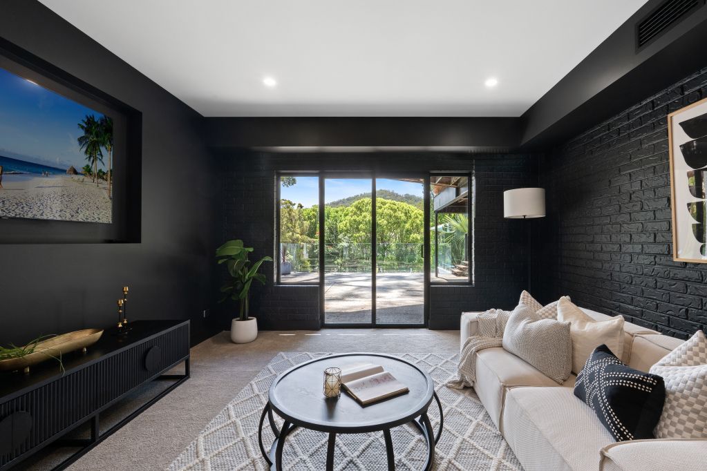 Modern black living room with white sofa, round coffee table, and glass doors to a sunny patio.